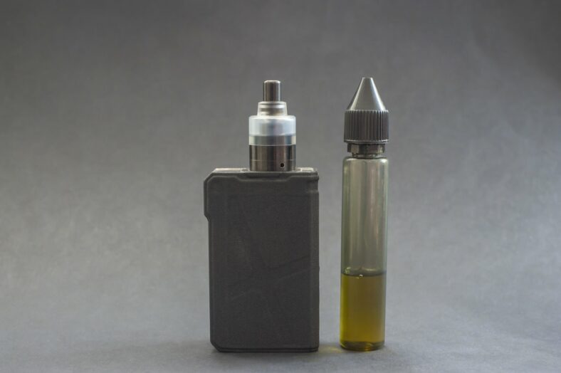 Ein Verdampfergerät links, daneben eine Flasche mit E-Liquid in einer transparenten Verpackung.